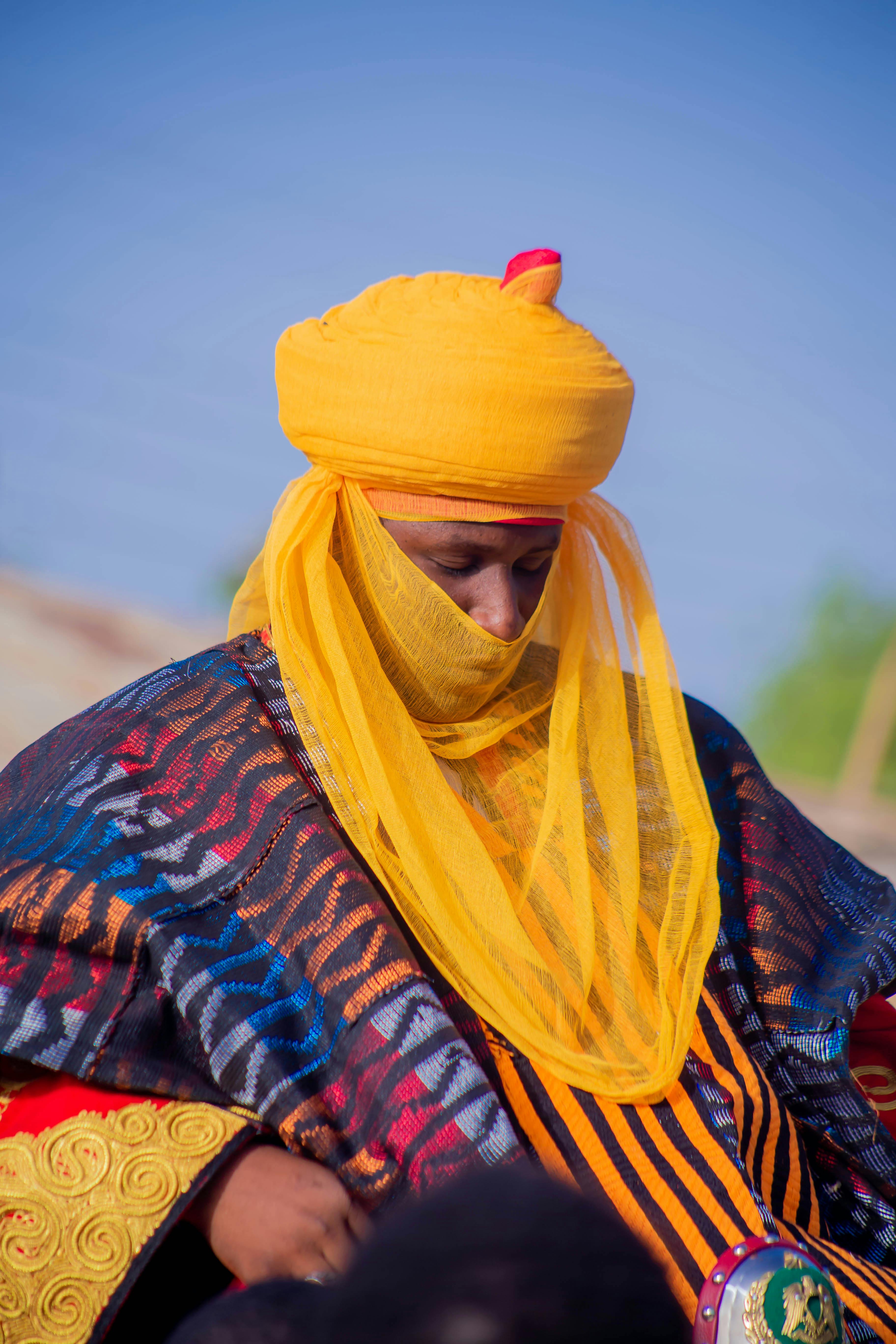 Man in colorful traditional clothing with a vibrant yellow headscarf outdoors.