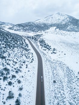 Aerial shot of a winding road cutting through a snowy mountain landscape. Winter scenery with clear skies.