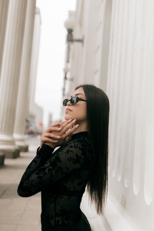 Free Fashionable woman in sunglasses poses beside white columns outdoors. Stock Photo
