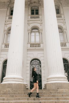 A woman in black walks past grand white columns of a historic building.