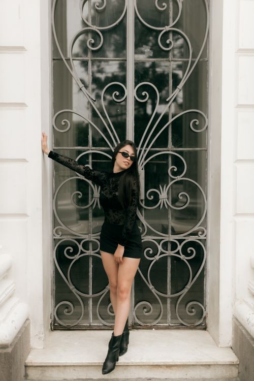 Free Chic woman in black outfit poses stylishly by a decorative iron gate outdoors. Stock Photo