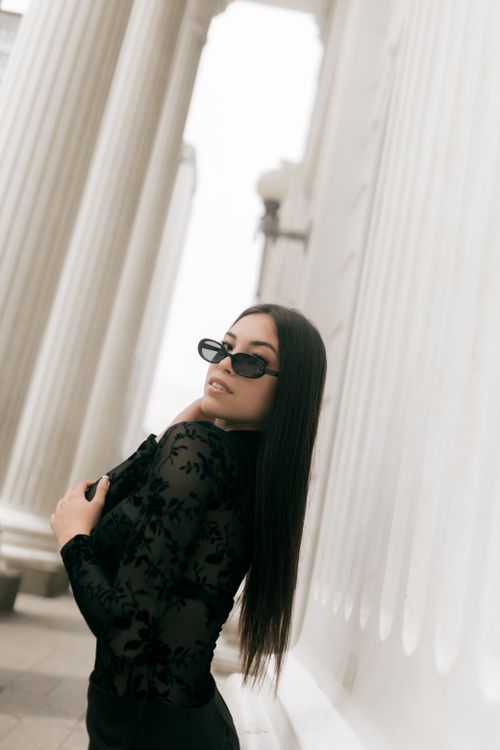 Free Elegant woman in black outfit and sunglasses posing by white classical columns. Stock Photo