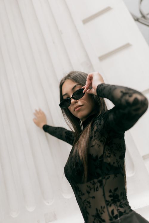 Free Fashionable woman in black lace outfit and sunglasses posing stylishly indoors. Stock Photo