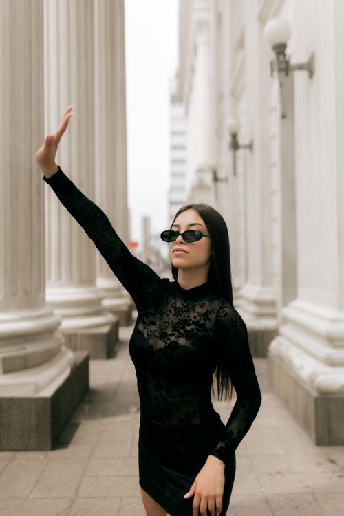 Free Chic woman in black dress and sunglasses posing confidently among tall columns. Stock Photo