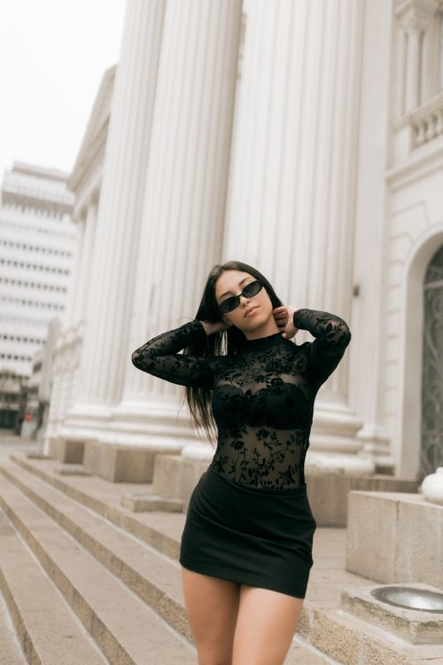 Free Stylish woman in black dress poses confidently in front of white pillars, exuding modern elegance. Stock Photo