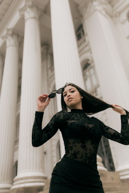 Free Confident woman in black dress posing with classical columns in the background. Stock Photo