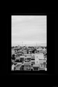 Black and white photo of urban rooftops through a window, creating a framed cityscape.