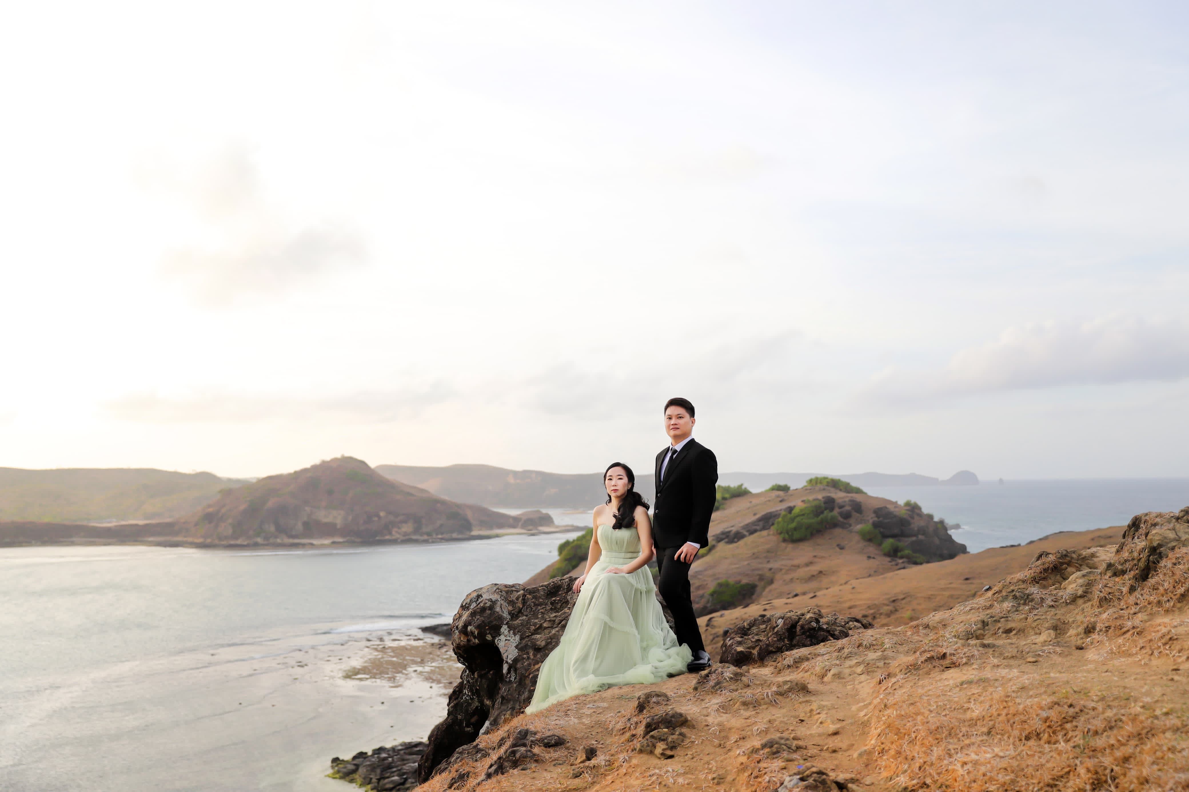 Couple in formal attire posing on a scenic cliff in Nusa Tenggara Barat, Indonesia.