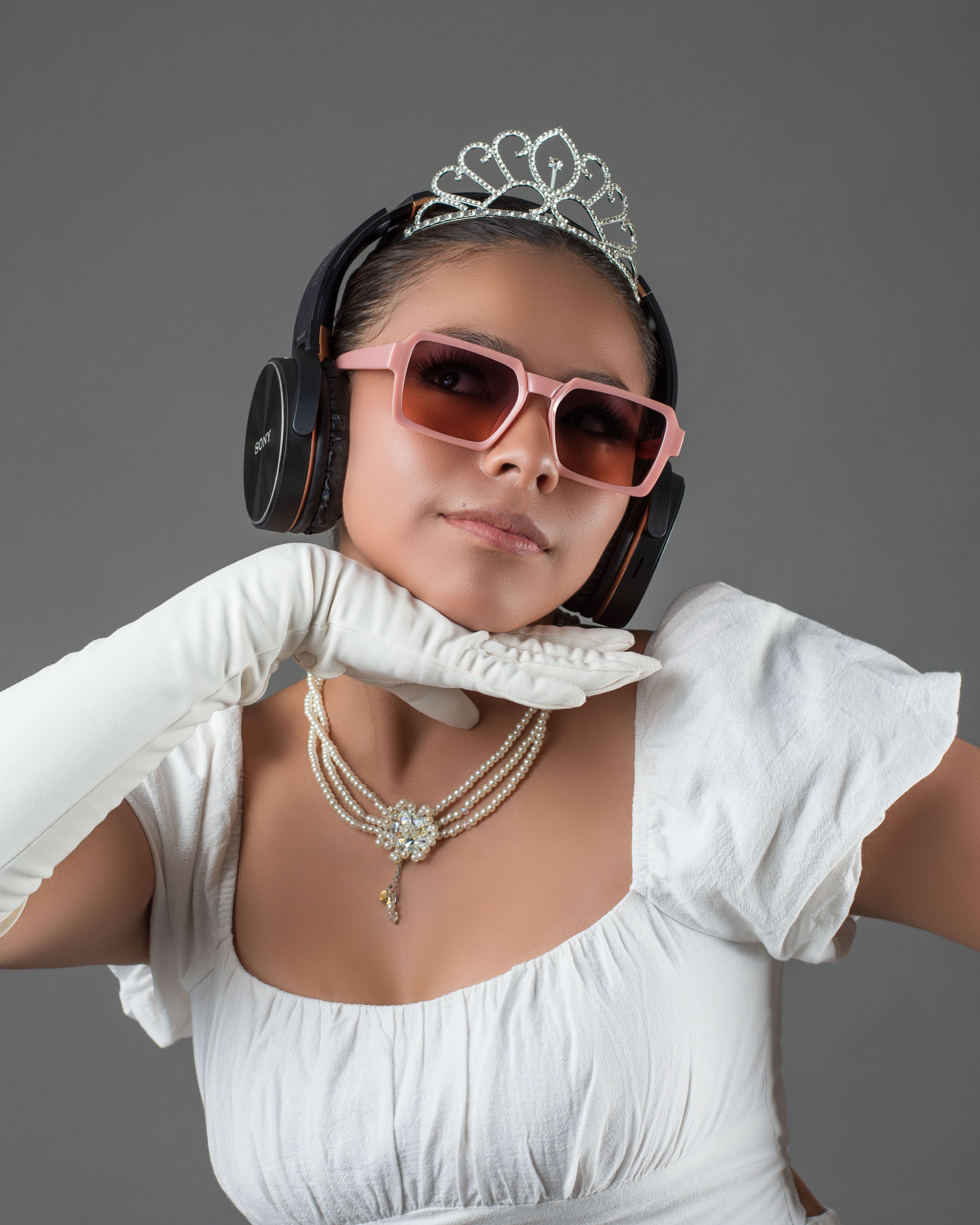 Fashionable woman wearing headphones, tiara, and sunglasses in studio setting. Elegant and modern.