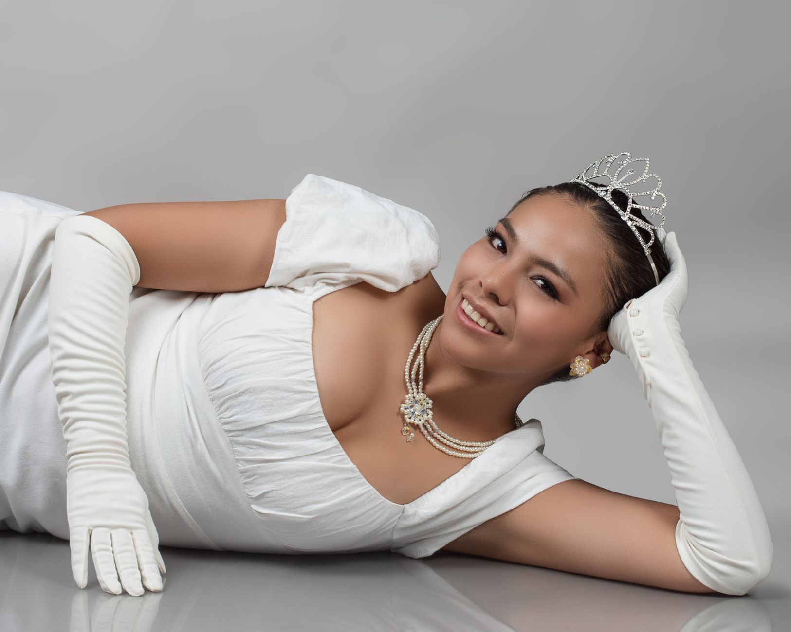 Portret van een lachende vrouw in een witte jurk en tiara, die elegantie en gratie uitstraalt.
