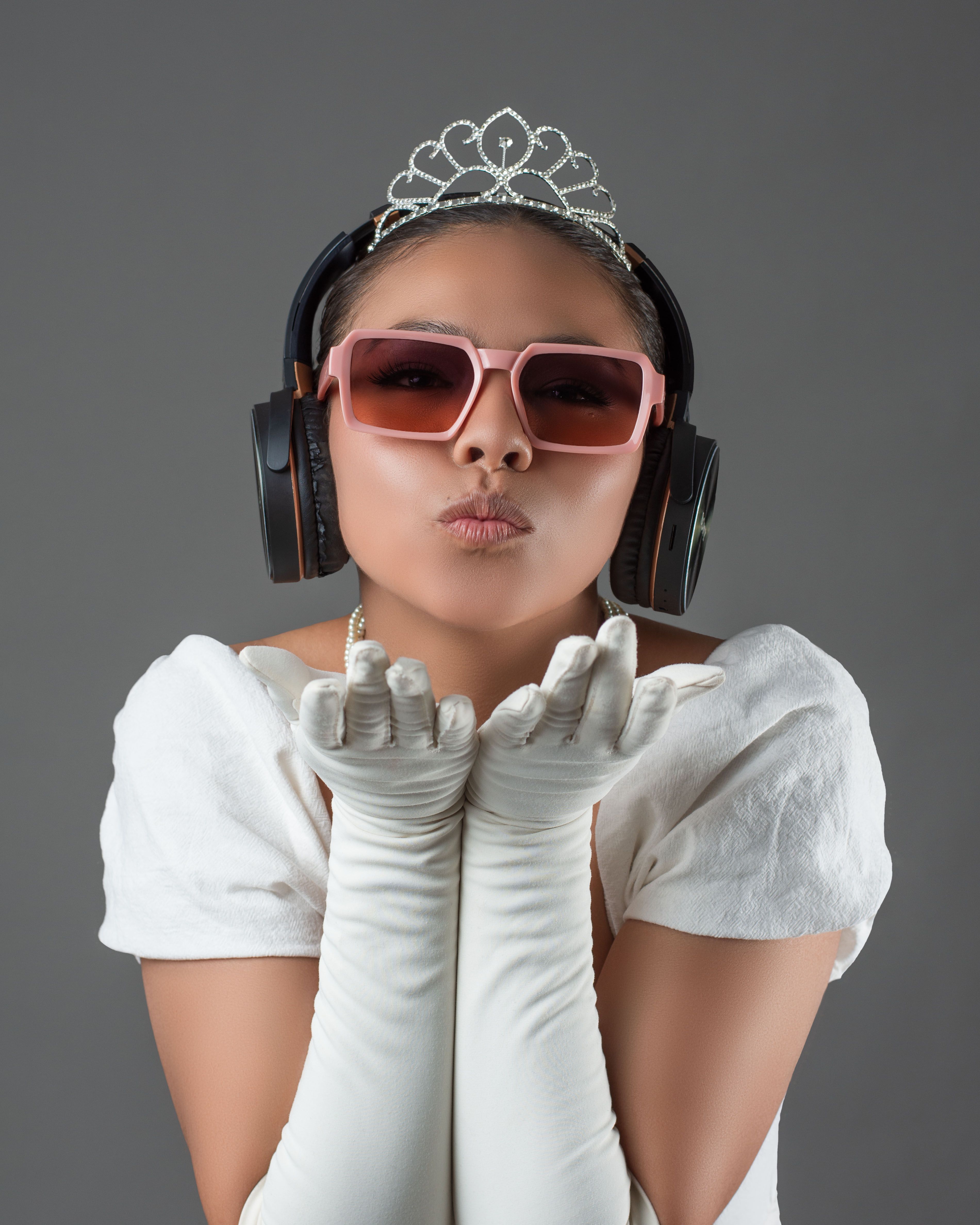 Stylish woman wearing tiara with headphones and sunglasses, blowing a kiss.