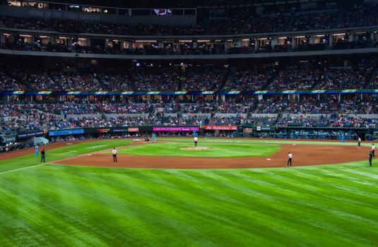 An engaging baseball game with a full crowd at Texas stadium under bright lights.