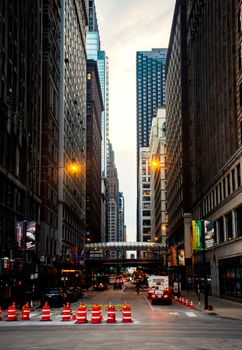 A busy urban street lined with tall skyscrapers during dusk, featuring traffic and city lights.