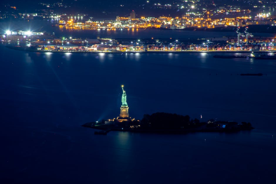 A stunning aerial view of the Statue of Liberty illuminated at night with city lights in the background.