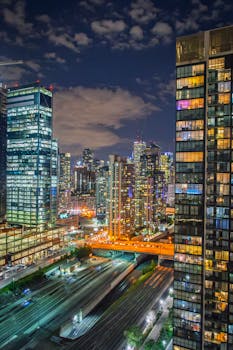 A stunning night view of a vibrant city skyline with illuminated skyscrapers and visible traffic below.