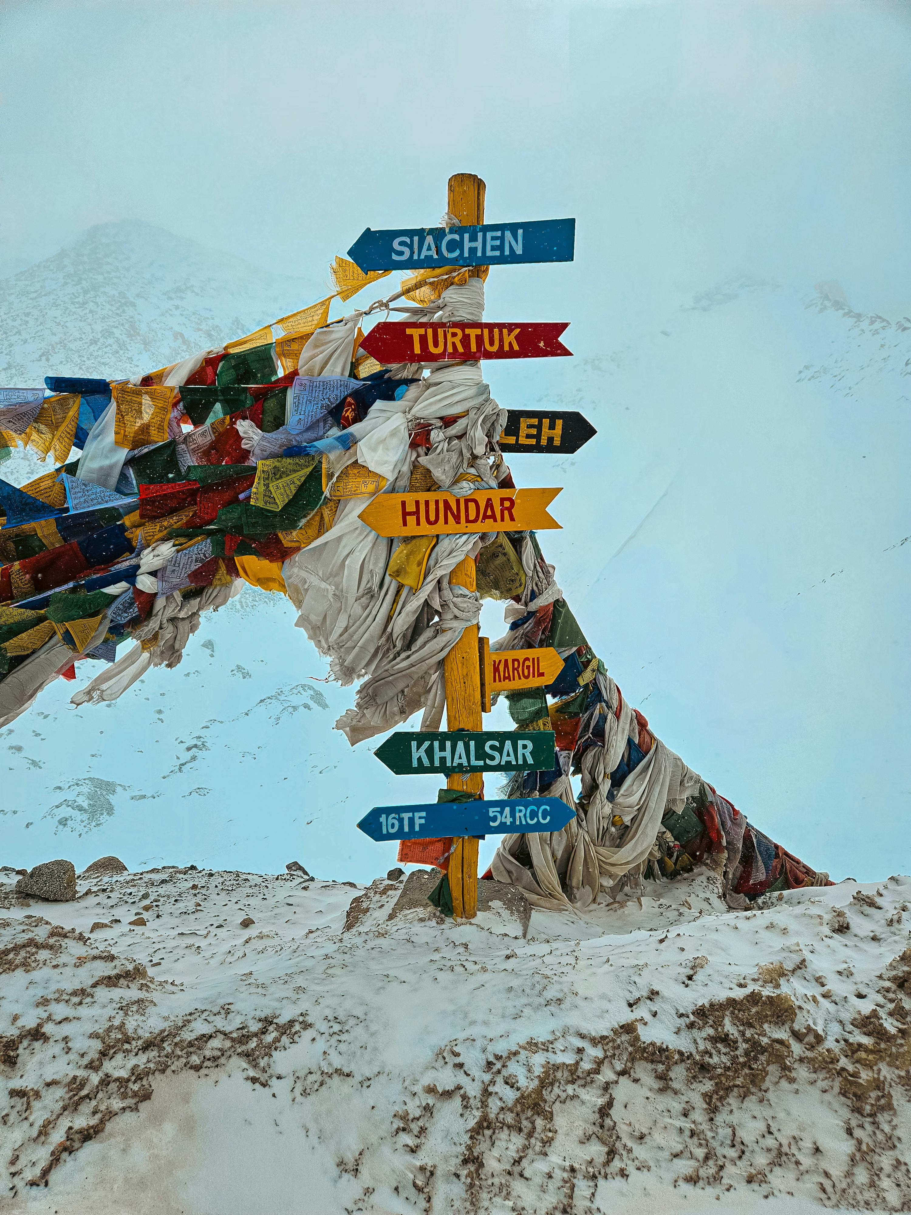 Vibrant signposts amidst snow in Khardung, Himalayas, surrounded by prayer flags.