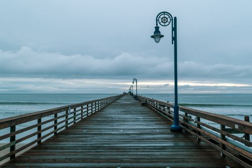 Free A tranquil view of a wooden pier extending into the ocean under a moody winter sky. Stock Photo