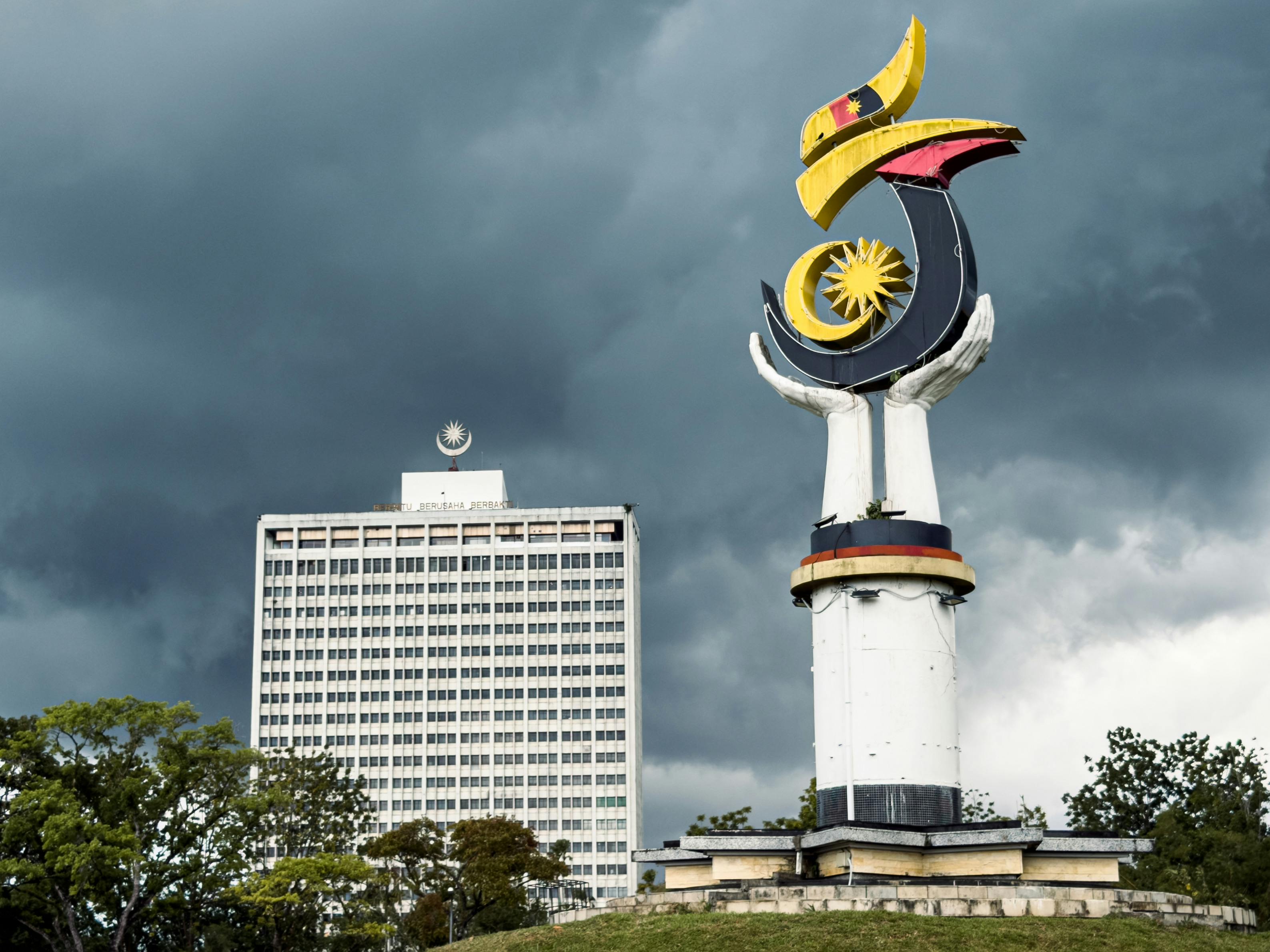 View of the unique monument and Wisma Bapa Malaysia building under dramatic clouds.