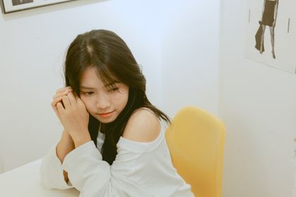 A young woman in casual attire sits thoughtfully indoors, conveying a serene mood — photo by Hồng Thắng Lê on Pexels