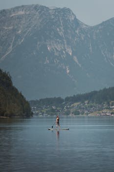 A person paddleboarding on a calm alpine lake with majestic mountain views under a clear sky.