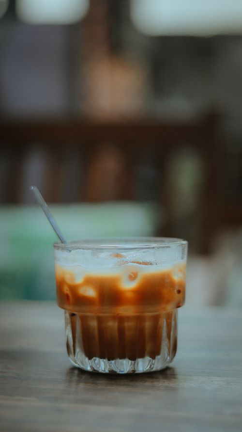 Free Close-up of an iced coffee in a glass with a straw on a wooden table, soft focus. Stock Photo