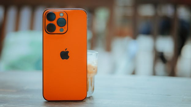 Orange smartphone with triple lens camera, standing on a table in a bright indoor setting.
