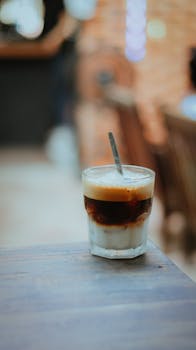 Close-up of an iced coffee with layers on a wooden table in a cafe setting.