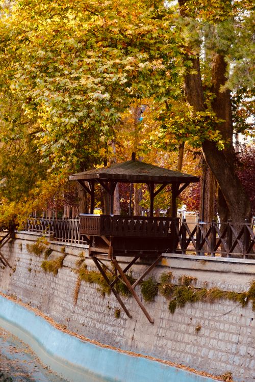 Free A charming wooden gazebo perched above a canal, surrounded by vivid autumn leaves. Stock Photo