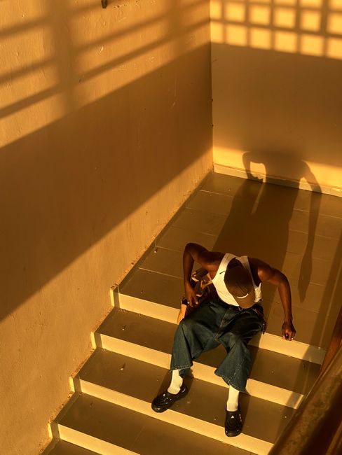 A man sits on stairs cast in dramatic shadow and warm light, creating a moody atmosphere.