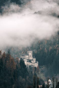 A mysterious castle enveloped by mist in a lush, autumnal mountain forest.