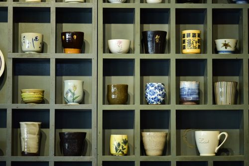 Free Collection of colorful ceramic mugs showcased on a wooden shelf in grid design. Stock Photo