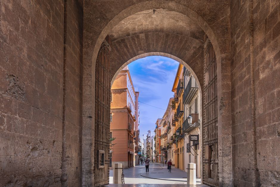 Explora una vibrante calle valenciana a través de un arco histórico bajo un cielo azul claro.