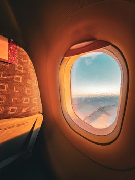 View from an airplane window with warm sunlight streaming onto the seat, capturing a serene sky view.
