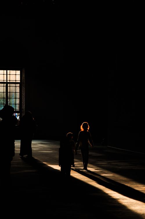 Free People walking in a dimly lit hall with a sunlit window casting shadows. Stock Photo