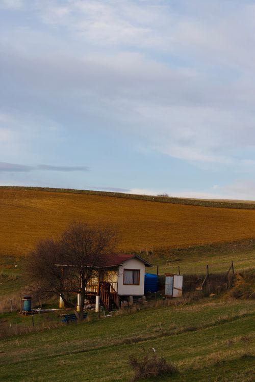 Free A lone cabin situated in expansive rural fields under a vast sky, capturing serene countryside beauty. Stock Photo