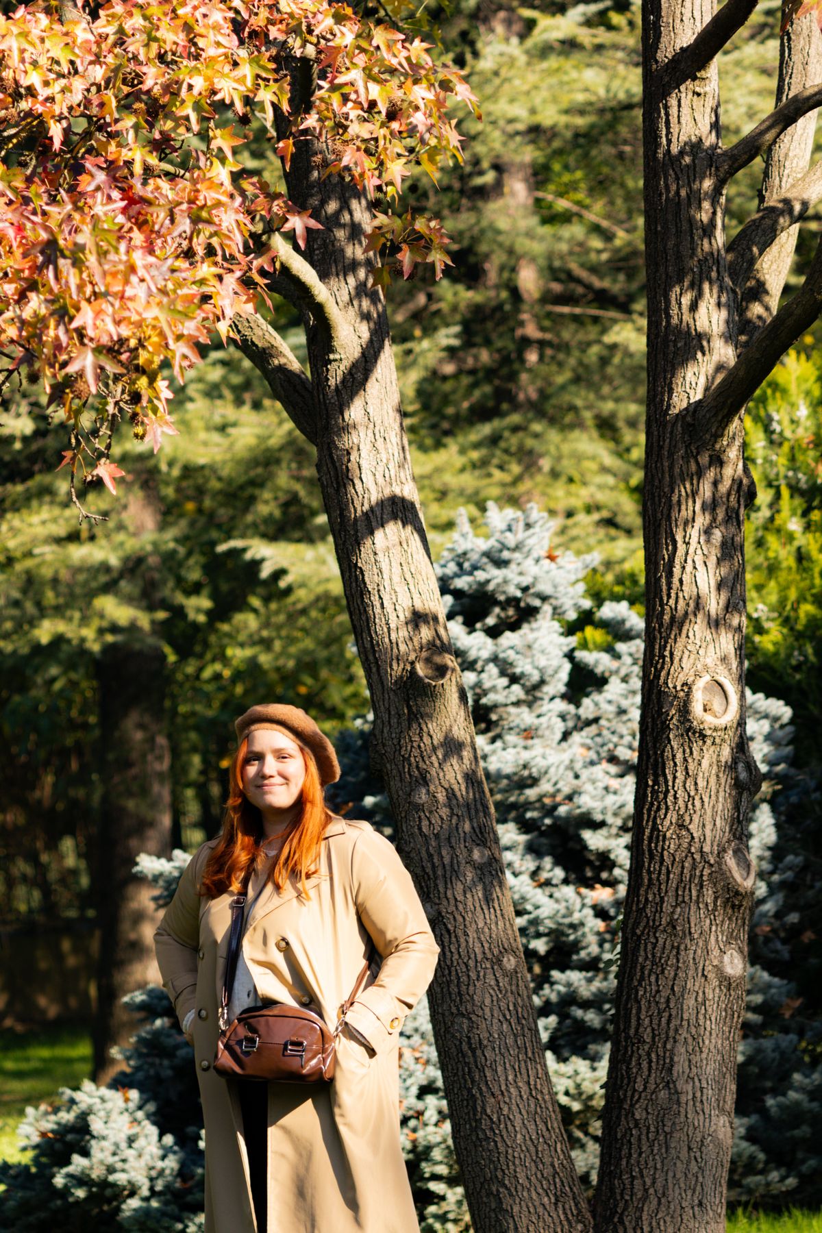 Woman dressed in a trench coat and hat enjoys a sunny autumn day outdoors.