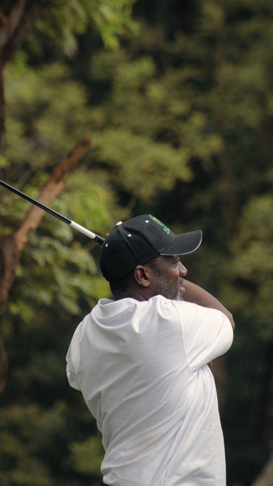 A golfer following through on his swing, framed by tall green trees
