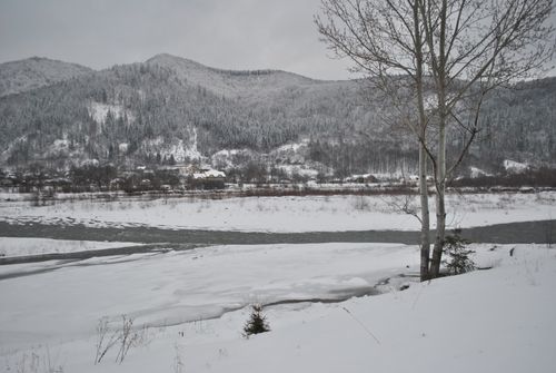 Free Serene winter scene of a river flowing through a snow-covered landscape with distant mountains. Stock Photo