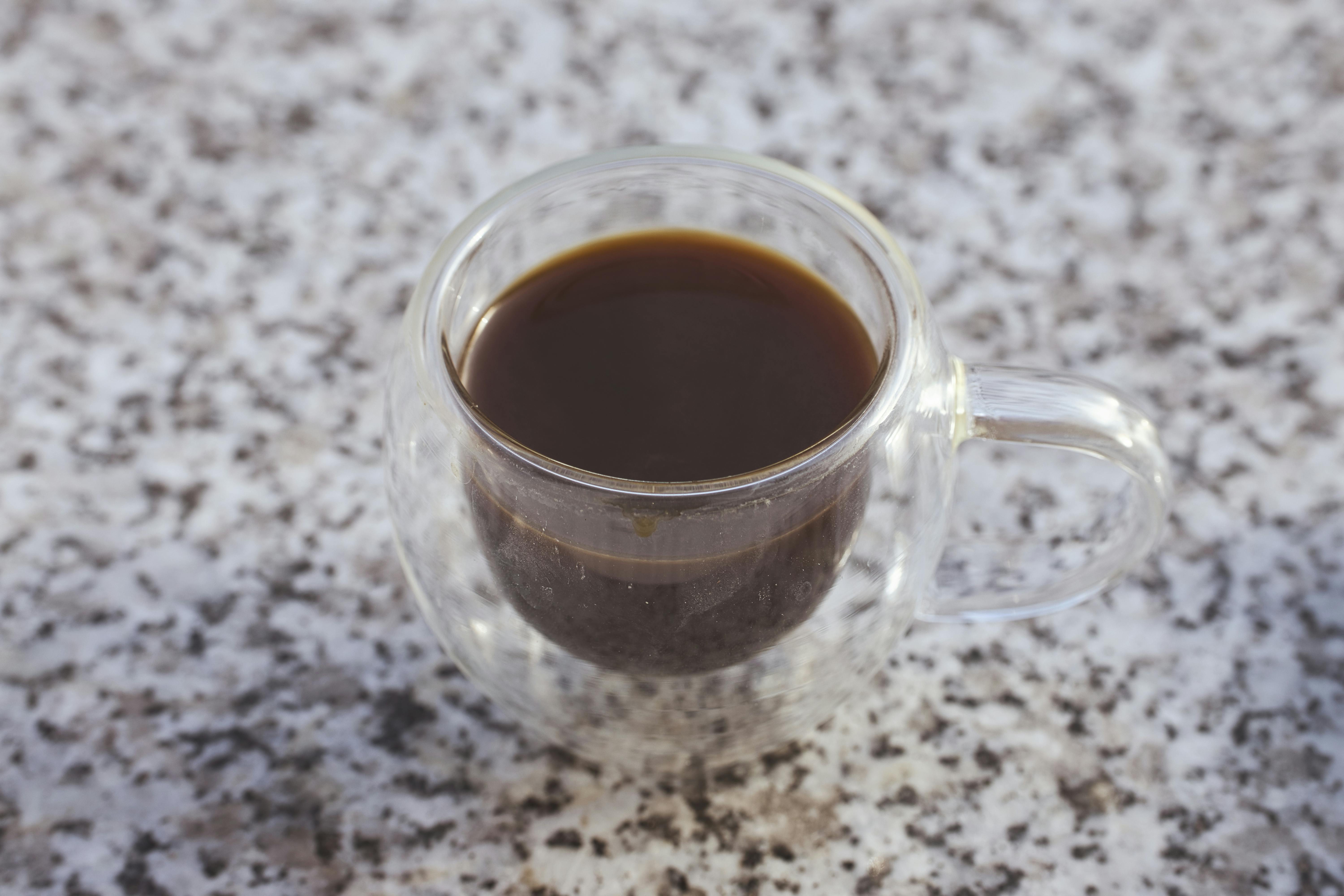 Close-up of black coffee in a glass mug on a speckled granite surface.