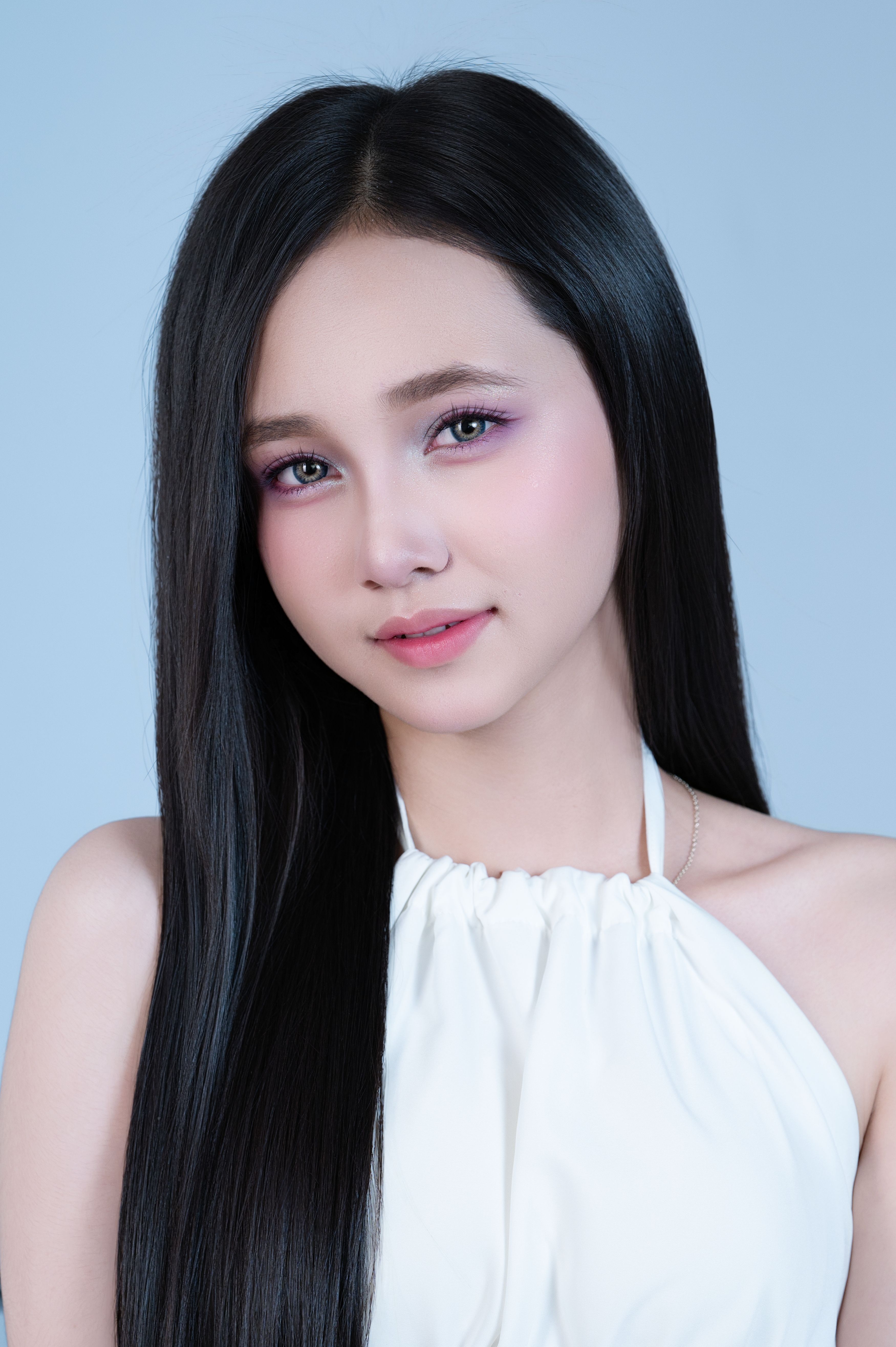 Beautiful young woman posing with long black hair and soft makeup against a light background.
