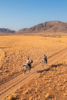 Two riders journey through an expansive desert landscape under a clear blue sky.