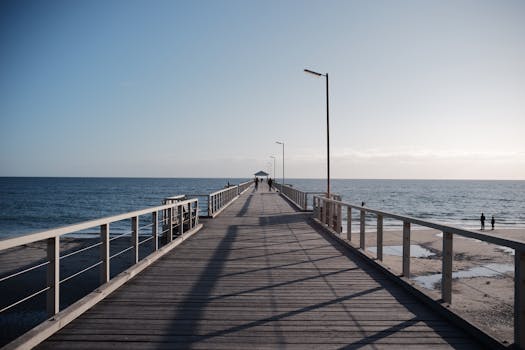 A wooden pier extends into the ocean under a clear sky, depicting a serene coastal scene.