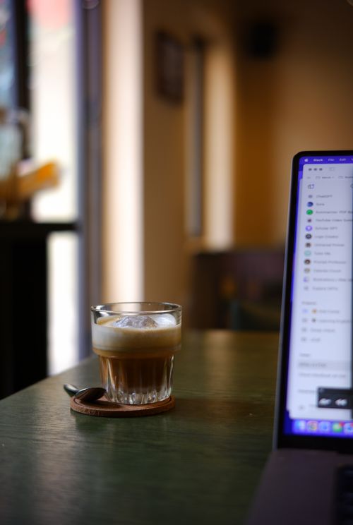 Free A warm, inviting cafe setting with a glass of coffee and a laptop, perfect for a work or leisure break. Stock Photo