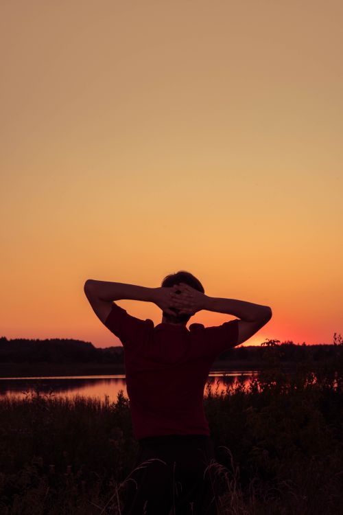 Free Silhouette of a person relaxing by a tranquil lake during a beautiful sunset. Stock Photo
