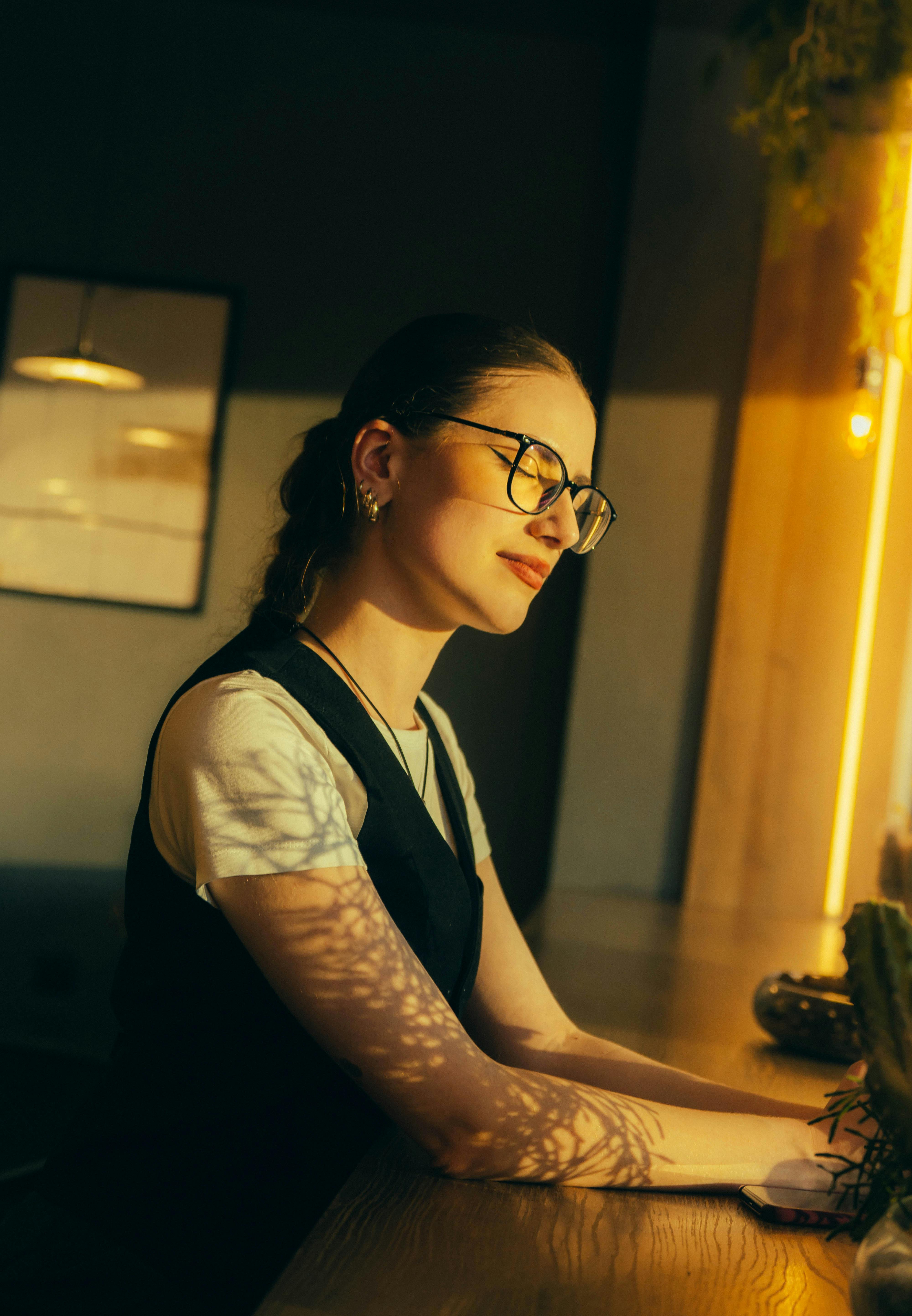 Kostnadsfria En kvinna sitter fridfullt vid ett fönster under gyllene timmen och solar sig i det varma solljuset. Stock foto