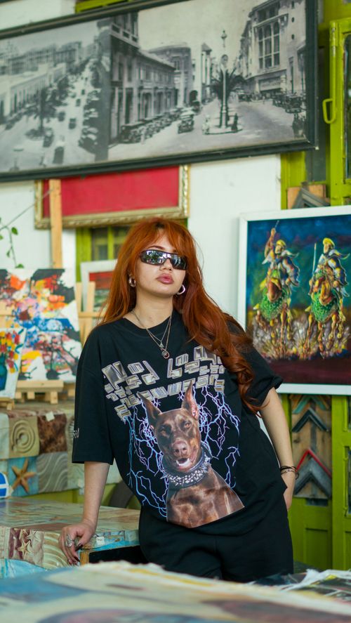 Free Woman in trendy attire poses in a vibrant art studio surrounded by colorful paintings and prints. Stock Photo