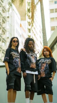 Three young adults showcase urban fashion against a Moroccan city backdrop, emphasizing modern streetwear.