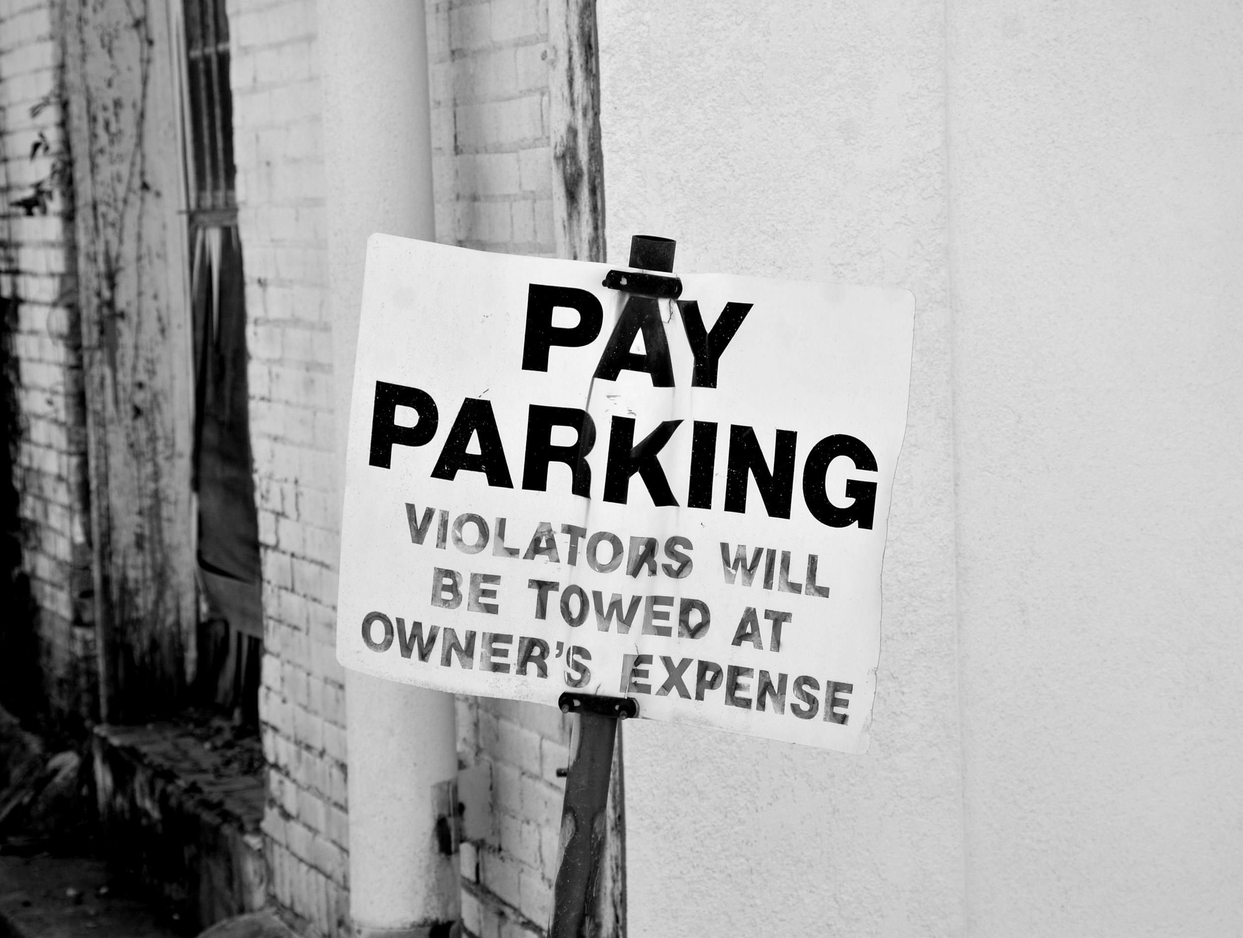 A black and white photo of a pay parking sign in downtown Tyler, Texas. Violators will be towed.
