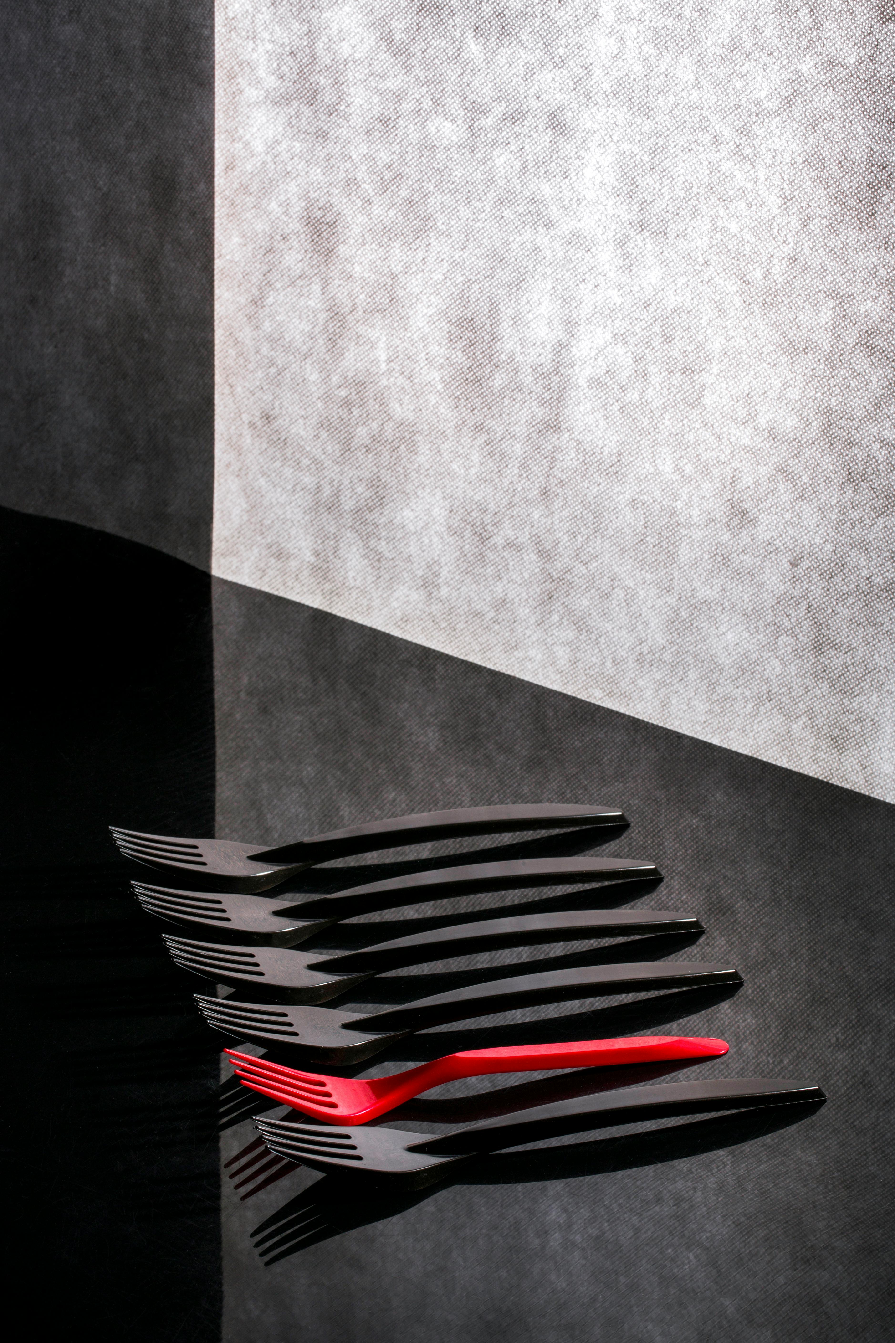 De franc Imatge espectacular de forquilles negres amb una forquilla vermella destacada sobre una superfície reflectant. Foto d'estoc