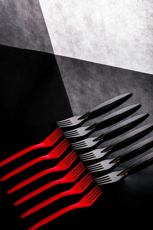 Free A creative and abstract display of red and black forks and knives on a textured background. Stock Photo